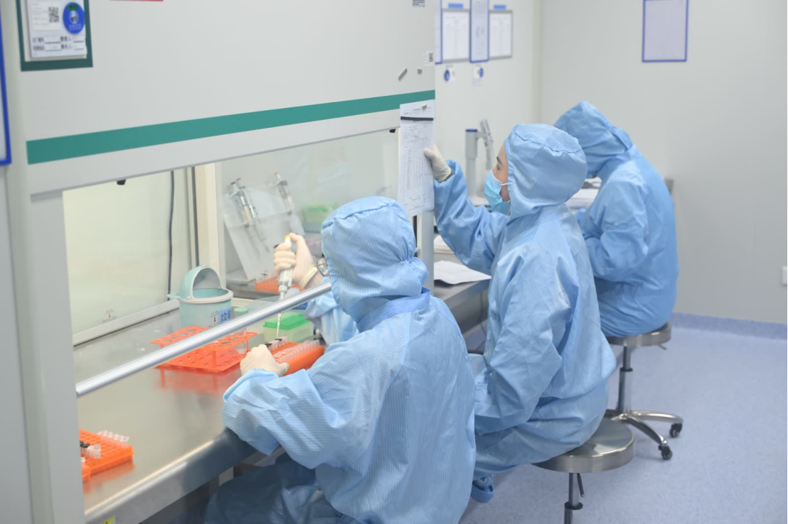 Laboratory personnel wearing protective clothing and performing molecular testing at a laboratory workstation